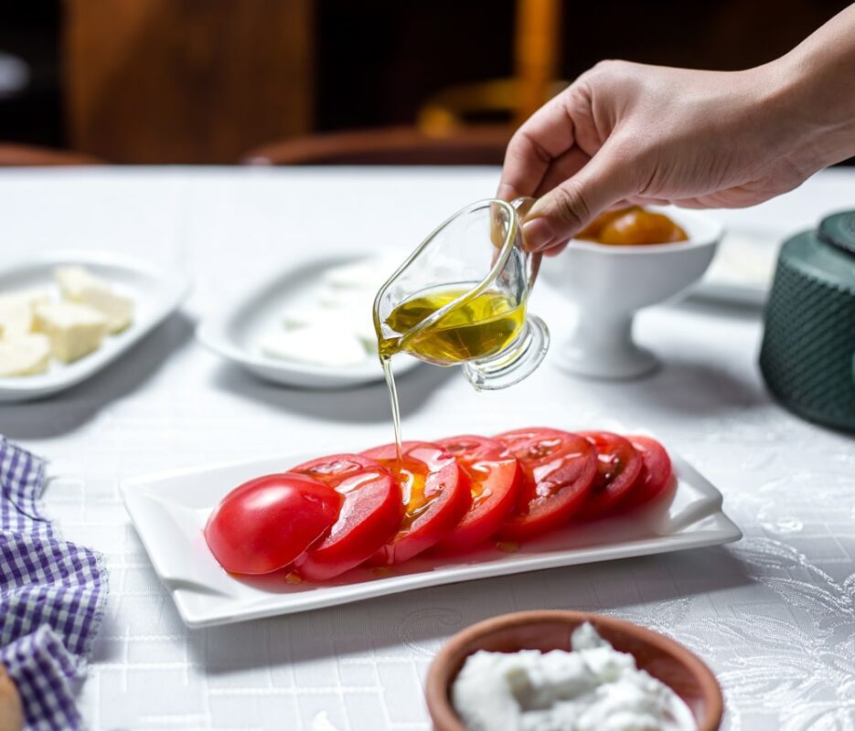 mann-gießt-olivenöl-geschnittene-tomaten-seitenansicht-min