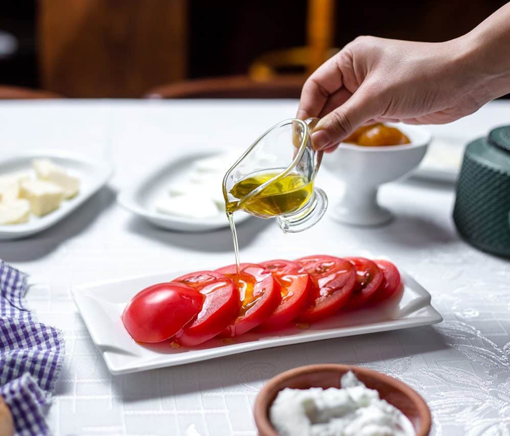 Mann-Gießt-Olivenöl-Geschnittene-Tomaten-Seitenansicht-Min